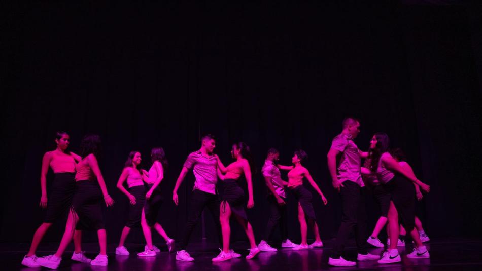 A group of dancers on a darkly lit stage.