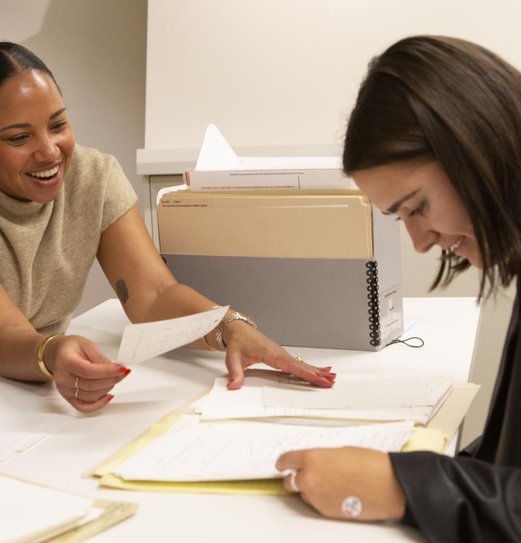 Two smiling women reading paperwork in an office.