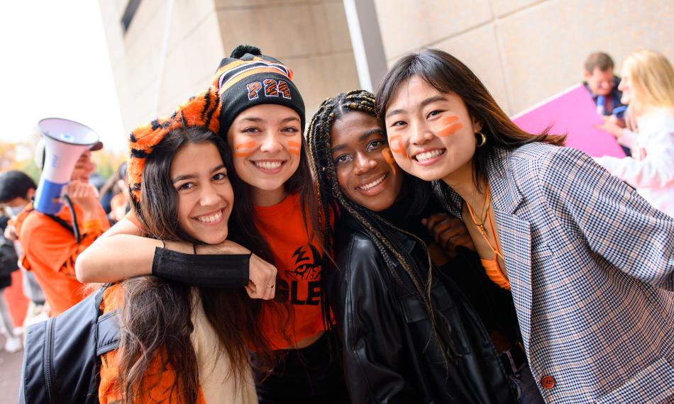 Four smiling female students wearing orange and black clothing