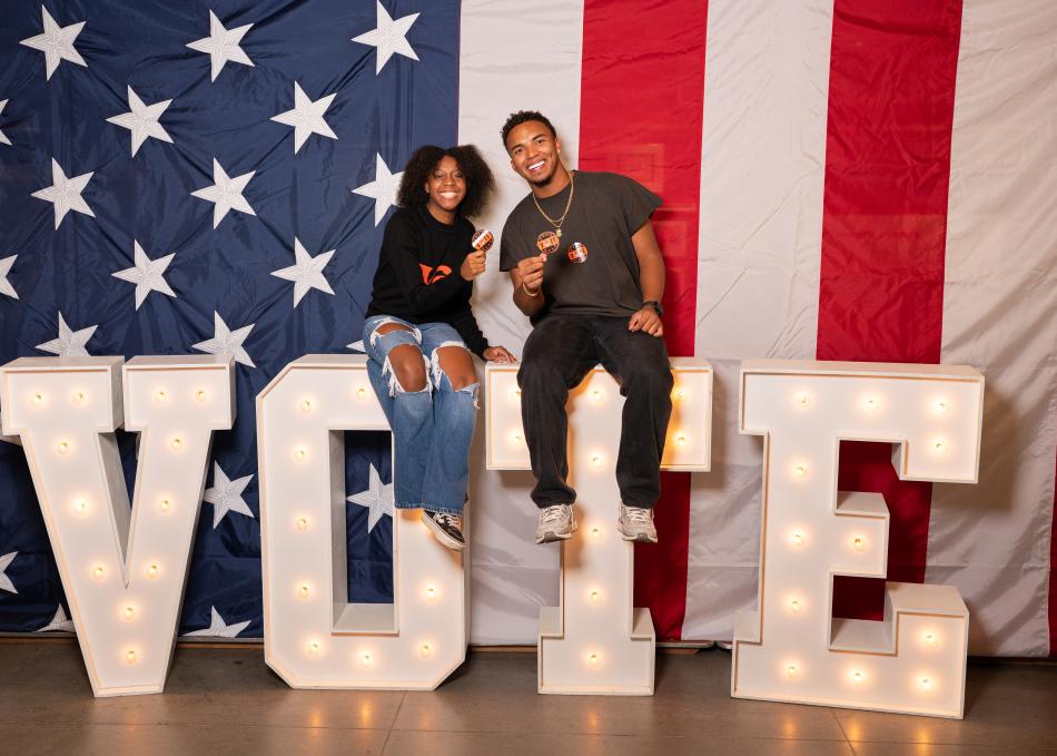 Students sitting on a sign that spells out Vote