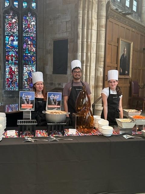 Three students in chef hats at a buffet table